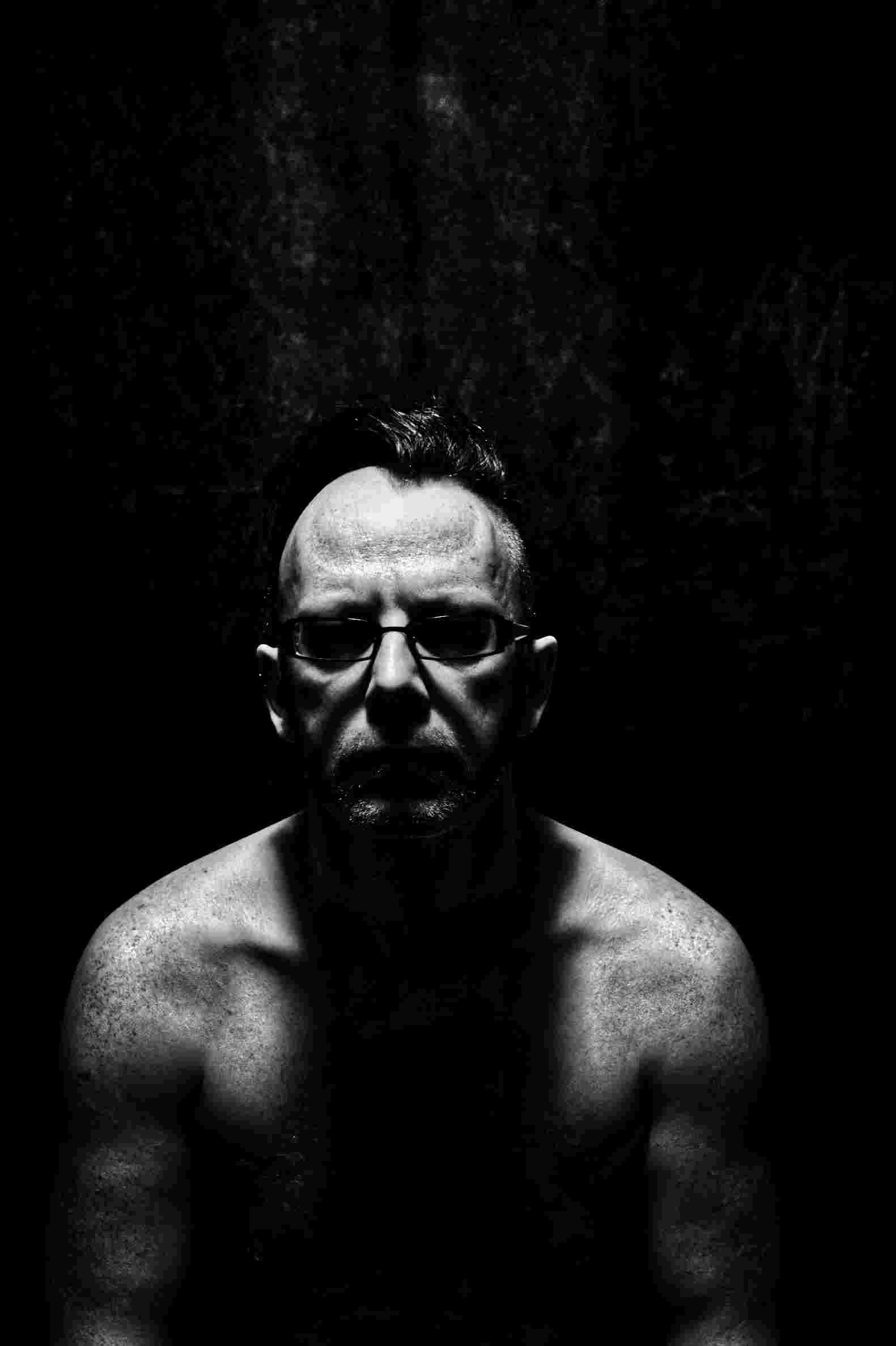 High contrast portrait of shirtless male agains black background