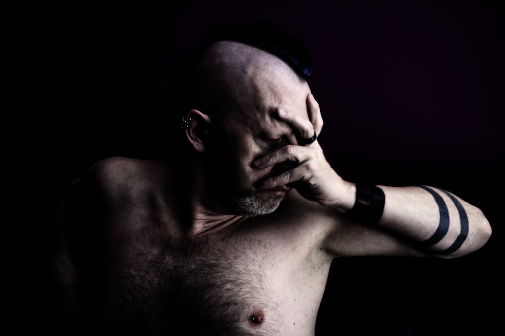 Portrait of shirtless male with tattoos holding one hand to face