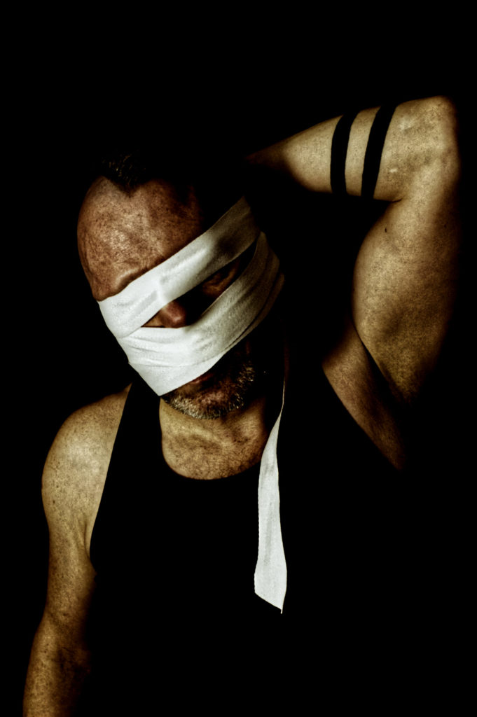 Male with bandages over eyes and mouth against black background